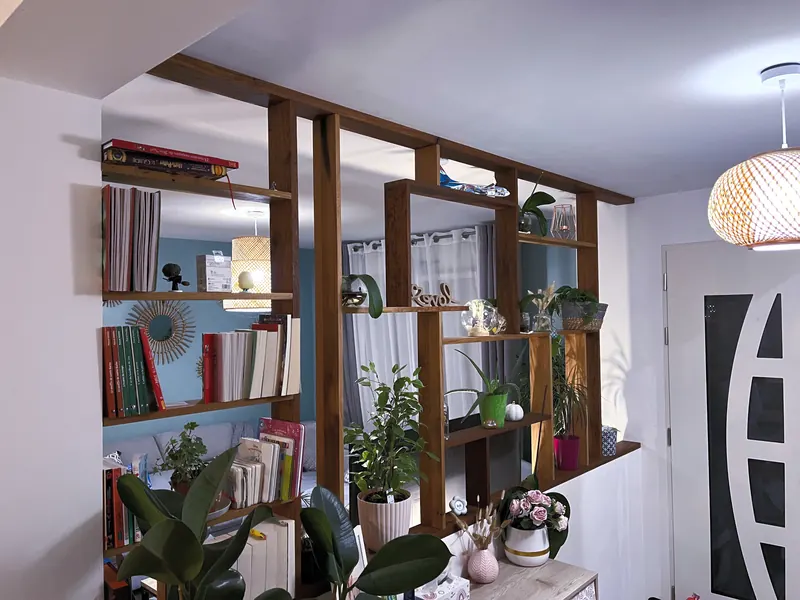 Bibliothèque claustra en bois séparant l’entrée du séjour, garnie de livres et de plantes